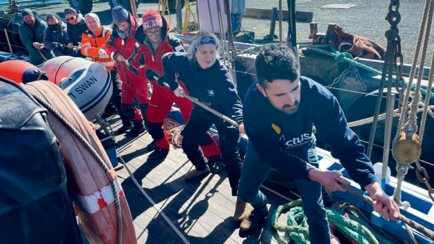 A row of people pulling a thick line on deck